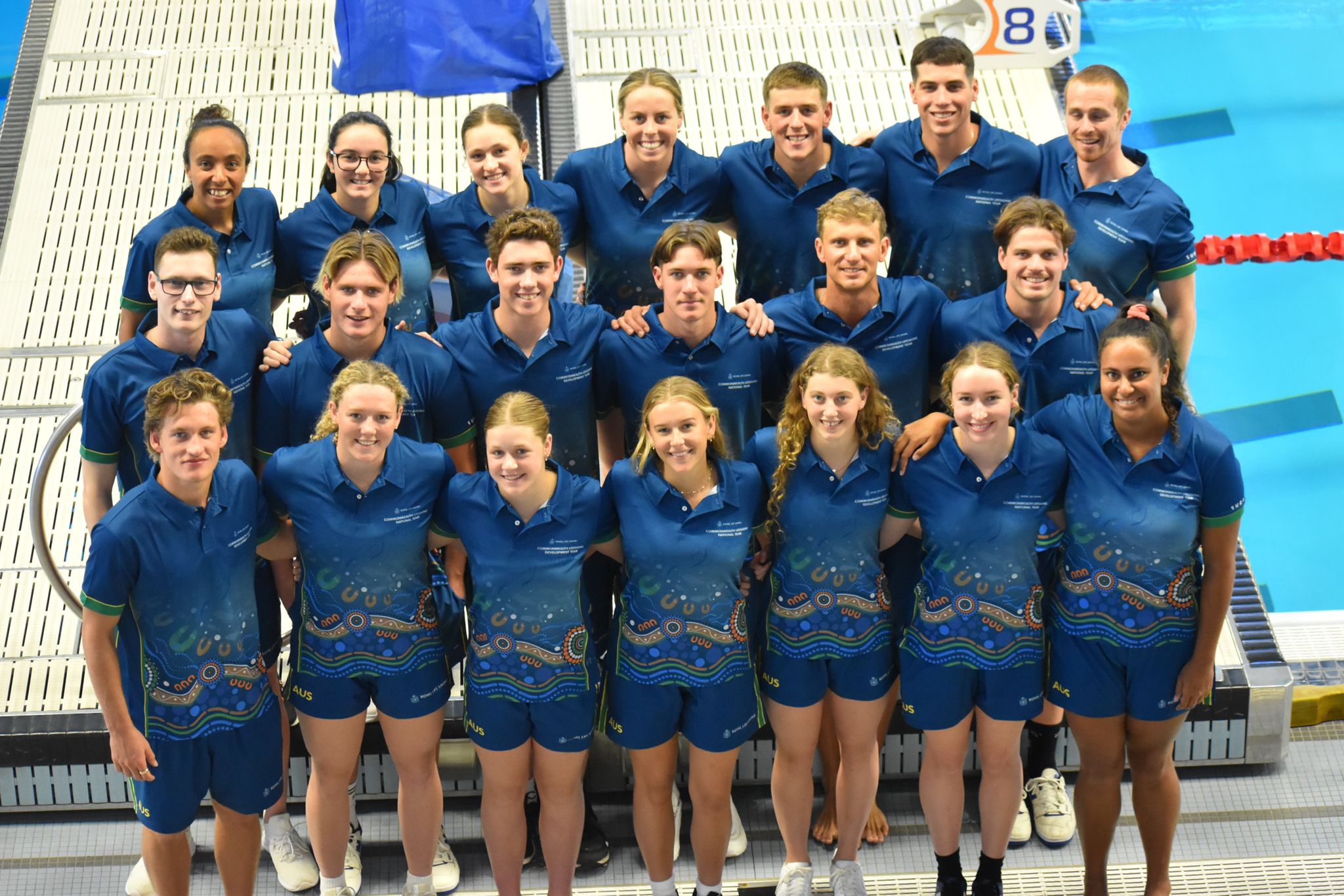 A photo of both Australian Teams together taken from above. There are three lines of people in their team unifroms standing in front of a pool.