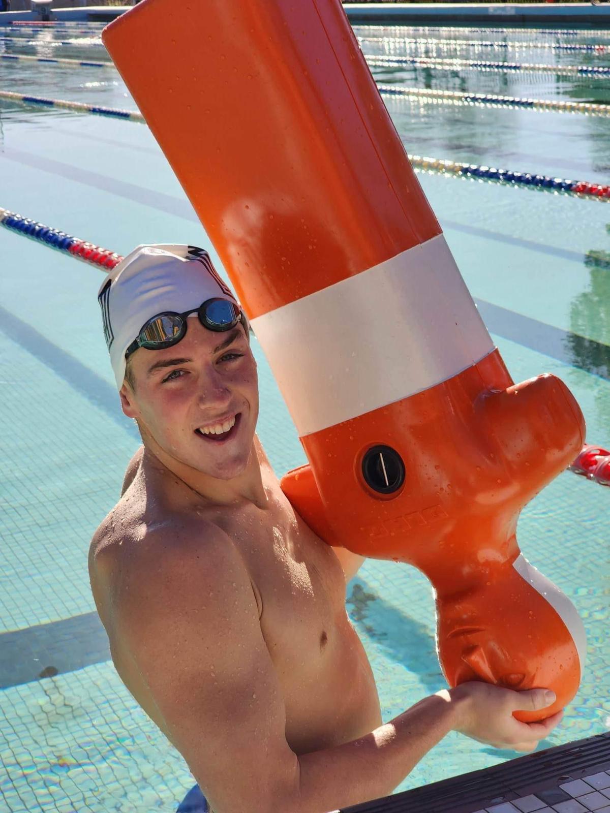 Brayden Woodford holding an orange mannikin while standing in a swimming pool.