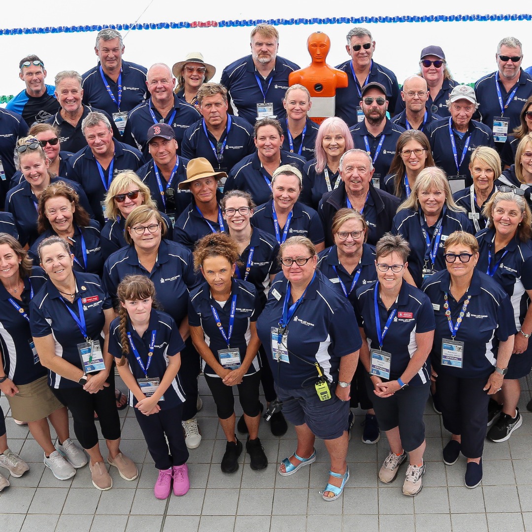 A group photo of Royal Life Saving - Australia Pool Life Saving Officials. All in their blue Royal Life Saving polo shirts, and standing in front of a swimming pool