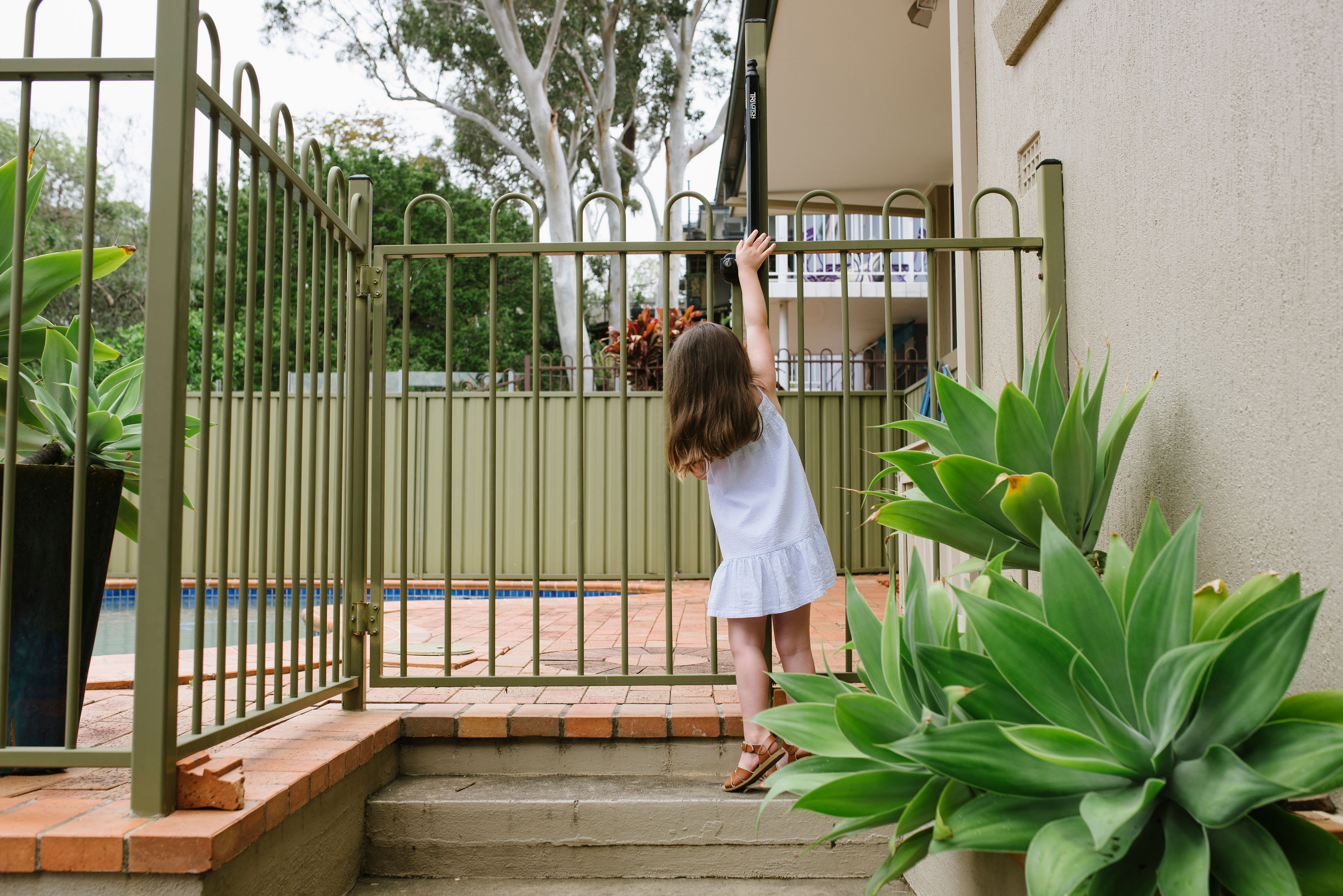 Child reaching up to undo pool gate