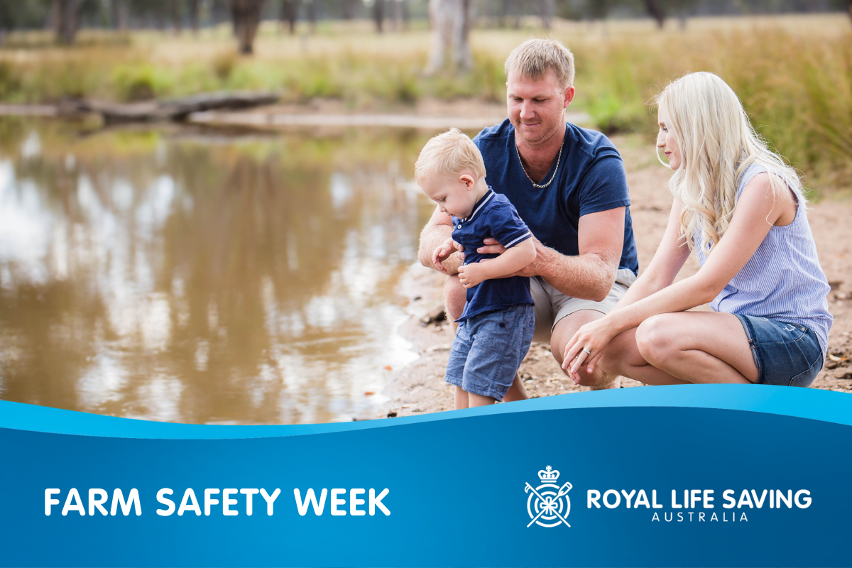 A man and a women crouch beside a lake, the man holds onto a toddler as he looks curiously at the water