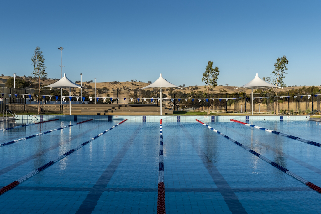 A photo of an outdoor swimming pool. The water is blue and the sky is a clear blue.